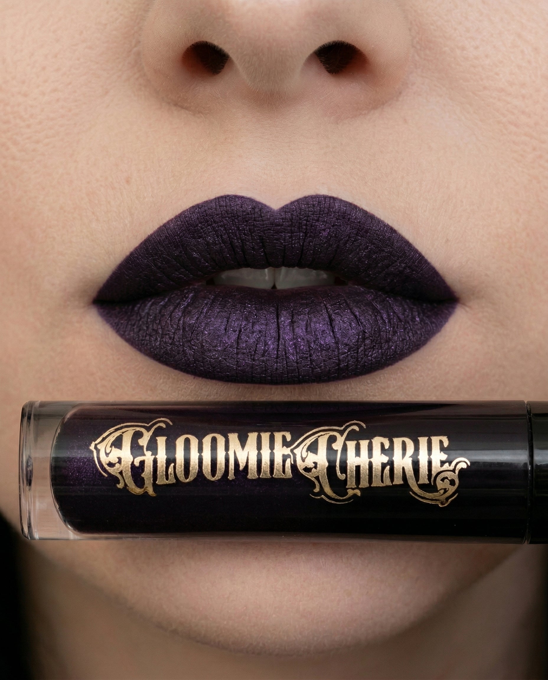 Close-up of a person wearing purple lipstick with a Gloomie Cherie lip product in the foreground.